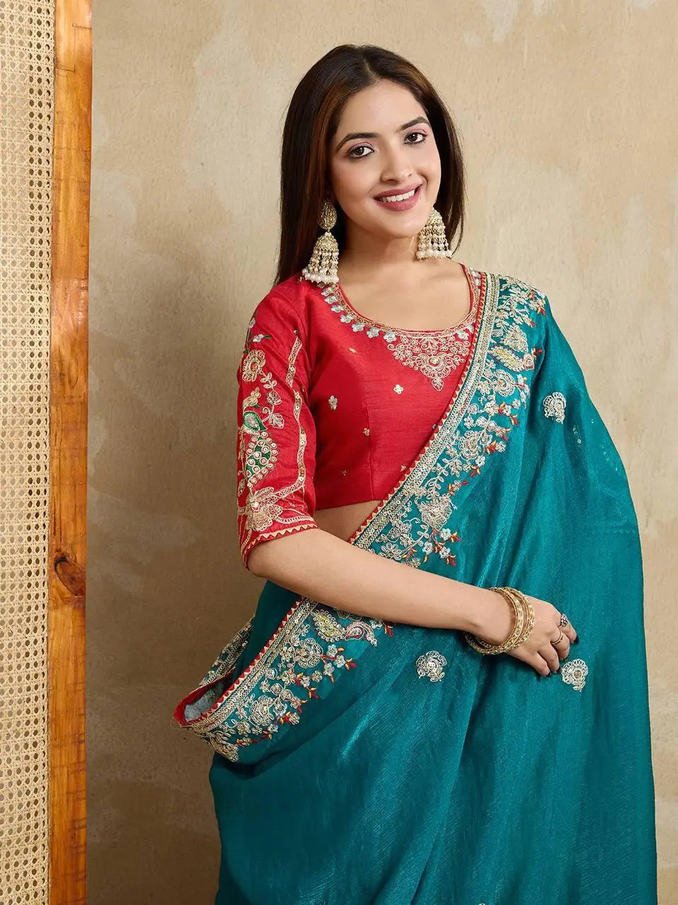 A woman models a vibrant Dark Pink Chiffon Silk Saree with scattered embellishments. The saree has a wide, intricate silver embroidery border. She wears a heavily embroidered dark green blouse and accessorizes with silver jewelry, posing indoors.